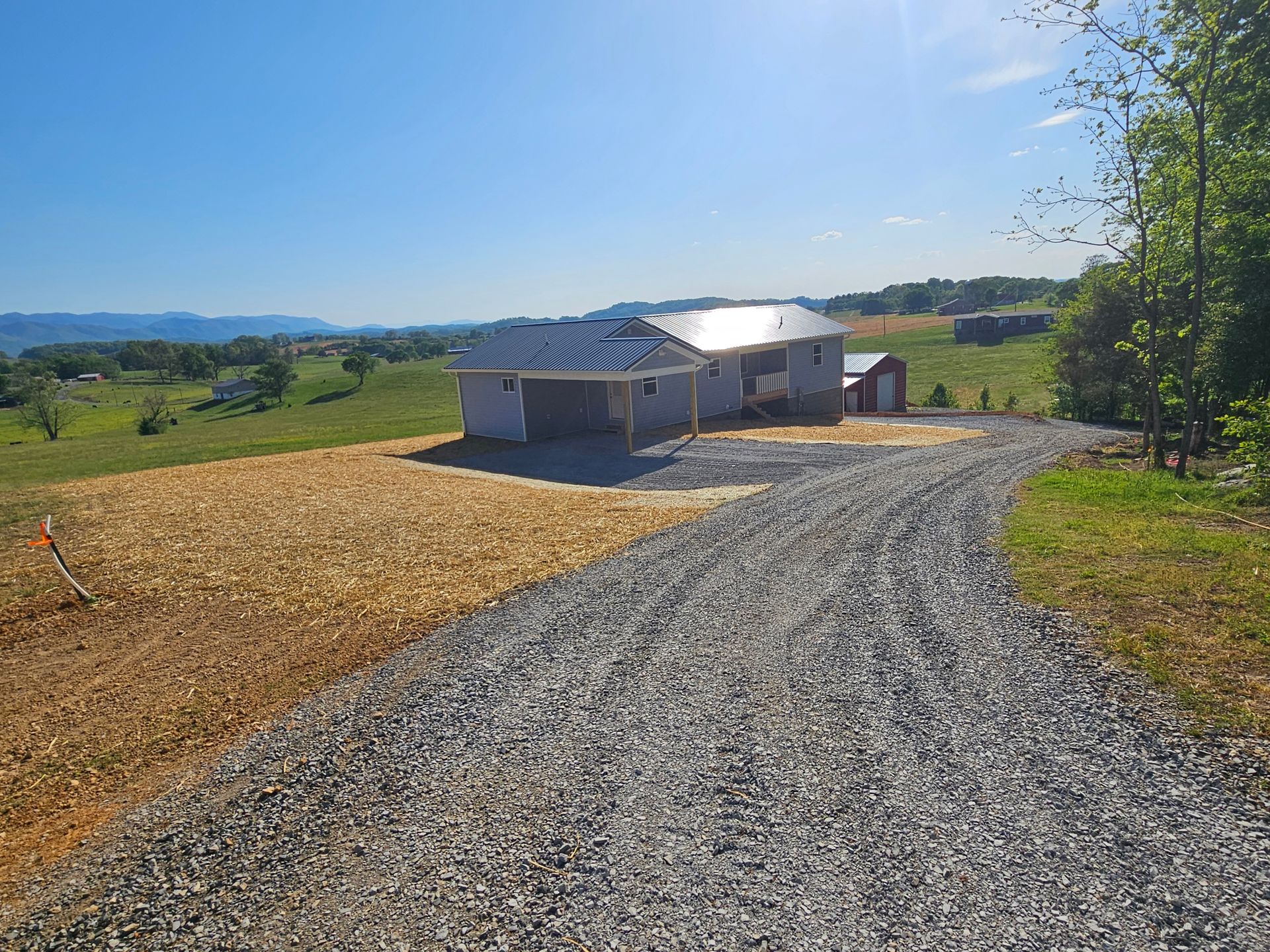 Gravel driveway leading to a house under construction in a sunny rural landscape