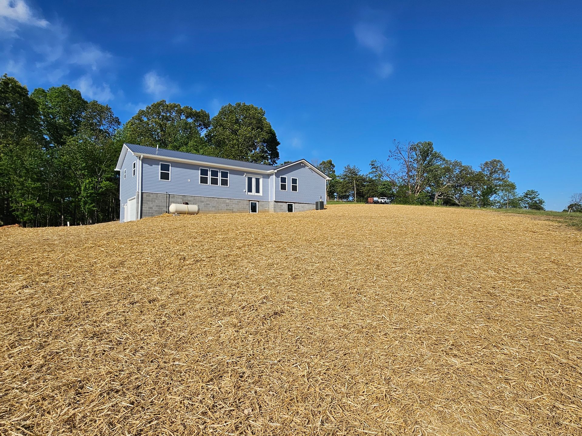 White house on a hill with a large tan gravel foreground and trees under a blue sky
