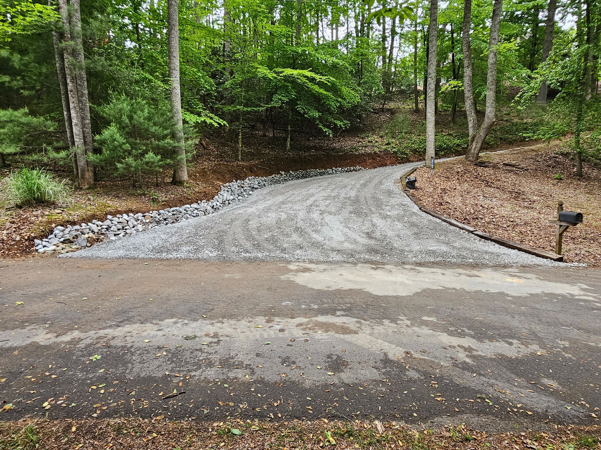 Gravel driveway curving into a wooded area, with trees and a small path light on the right.