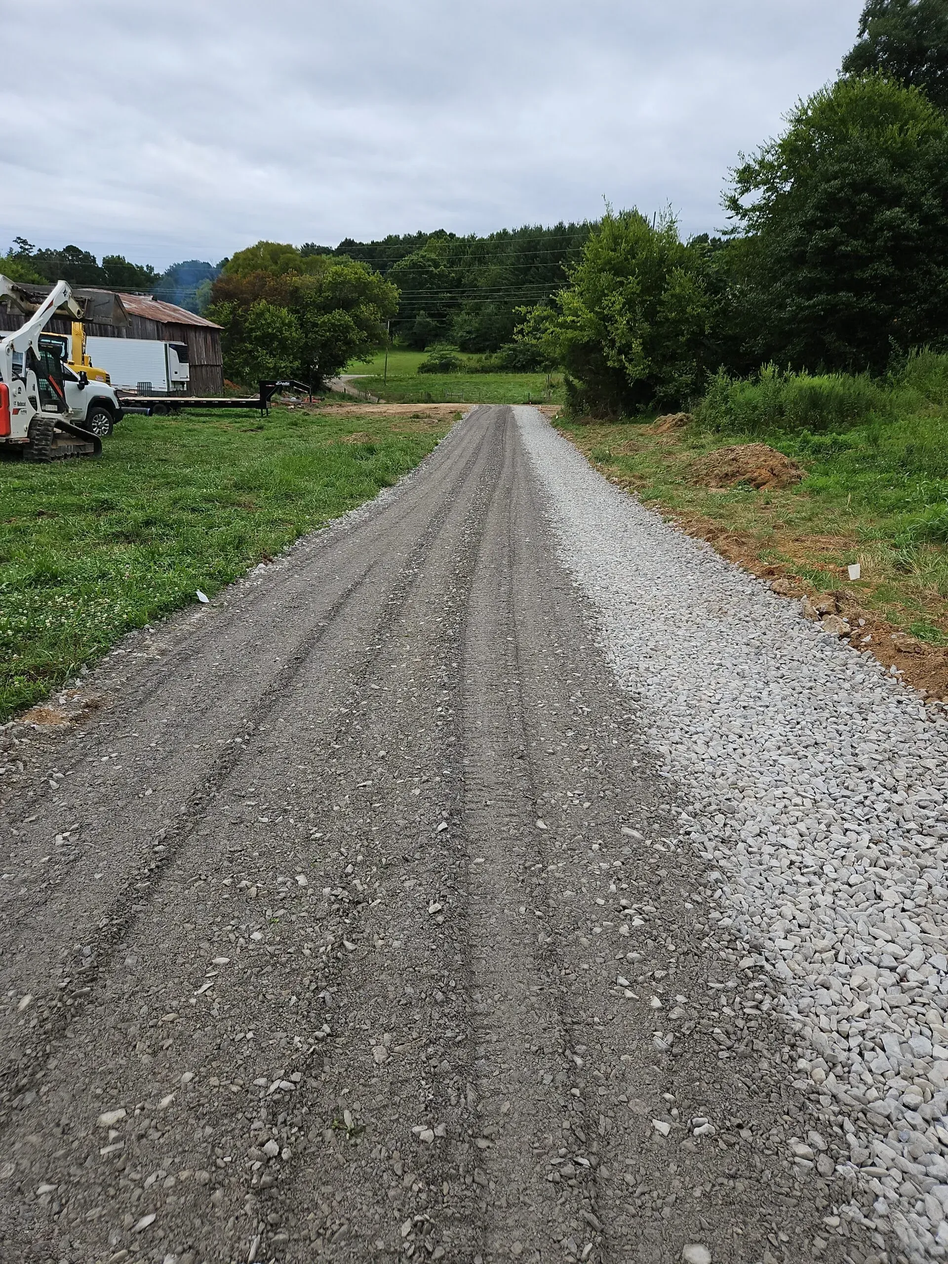 Gravel path through green fields toward trees under a cloudy sky
