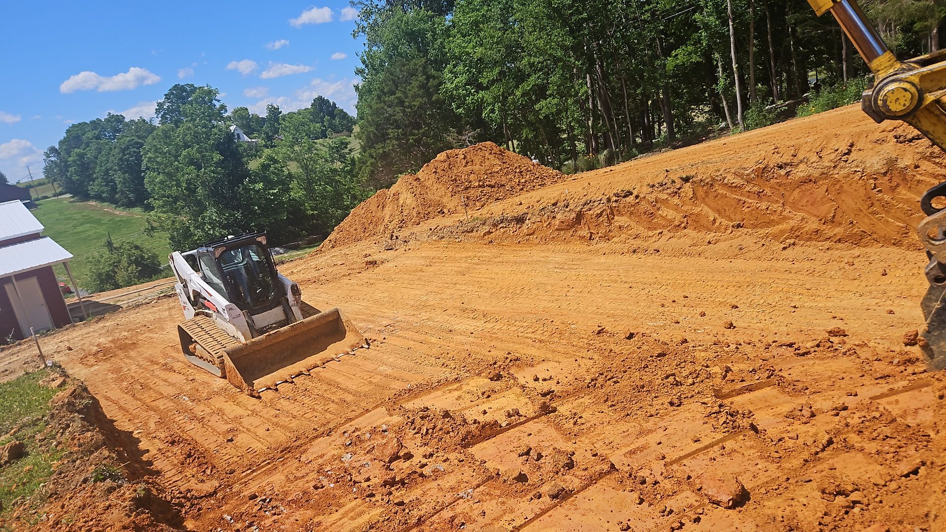 Bulldozer leveling orange dirt on a cleared construction site beside a wooded area