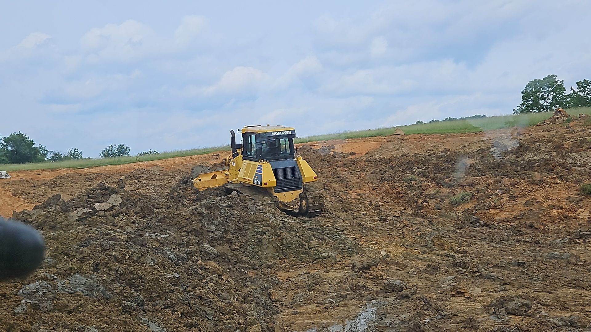 Yellow bulldozer working on a muddy dirt embankment under a cloudy sky