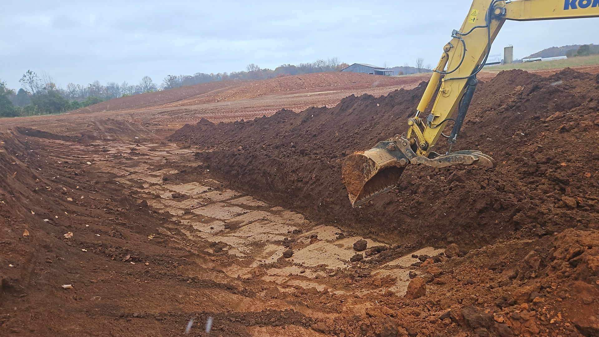 Excavator digging reddish dirt on a barren hillside construction site
