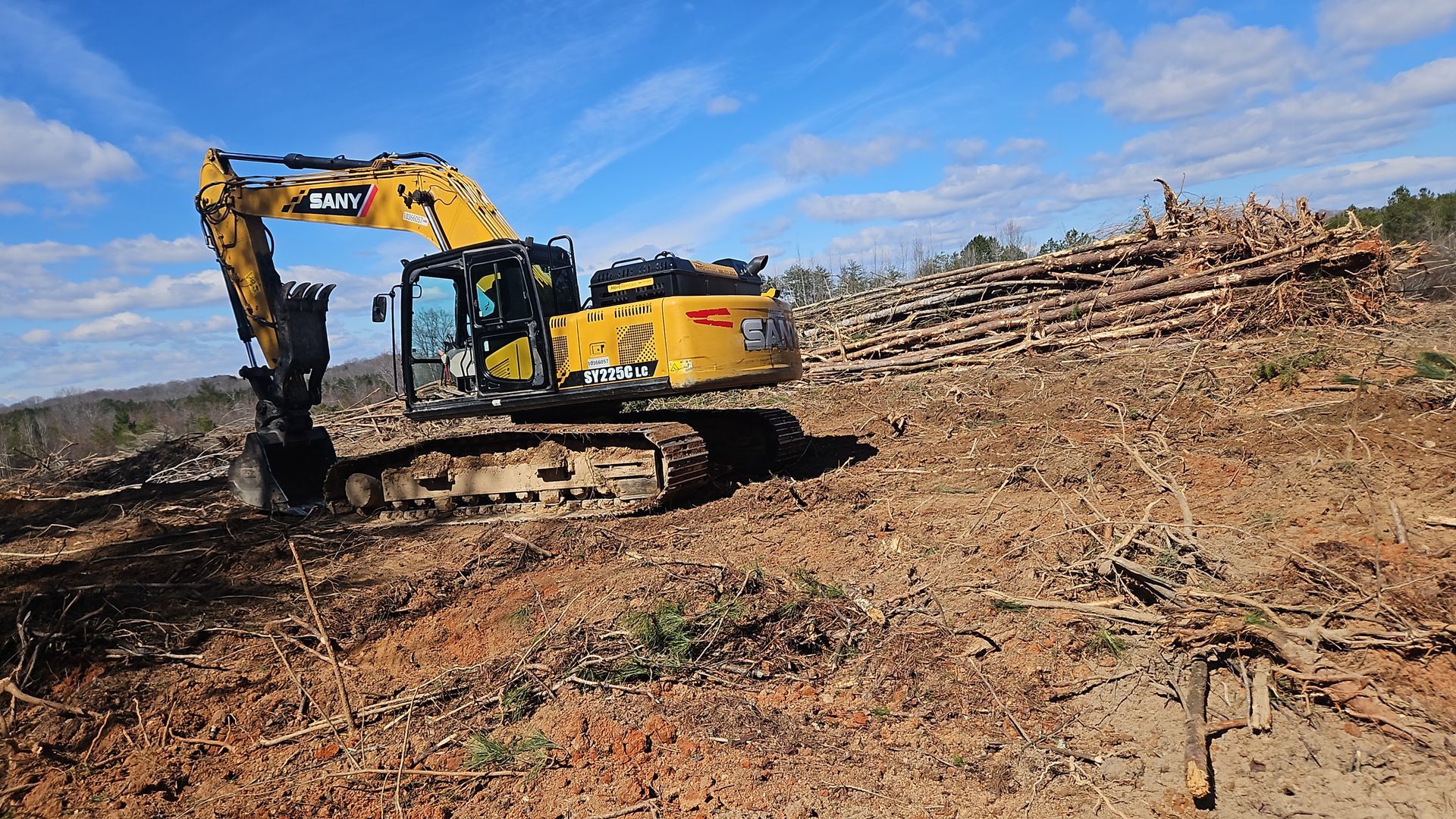 Yellow excavator clearing brush on a barren hillside under a clear sky