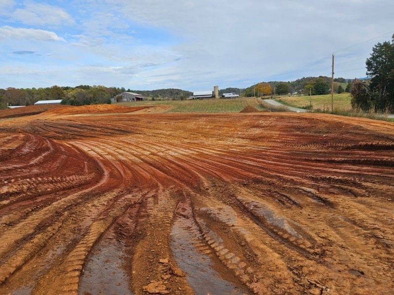 Red dirt construction site with tire tracks beside a rural road under a cloudy sky