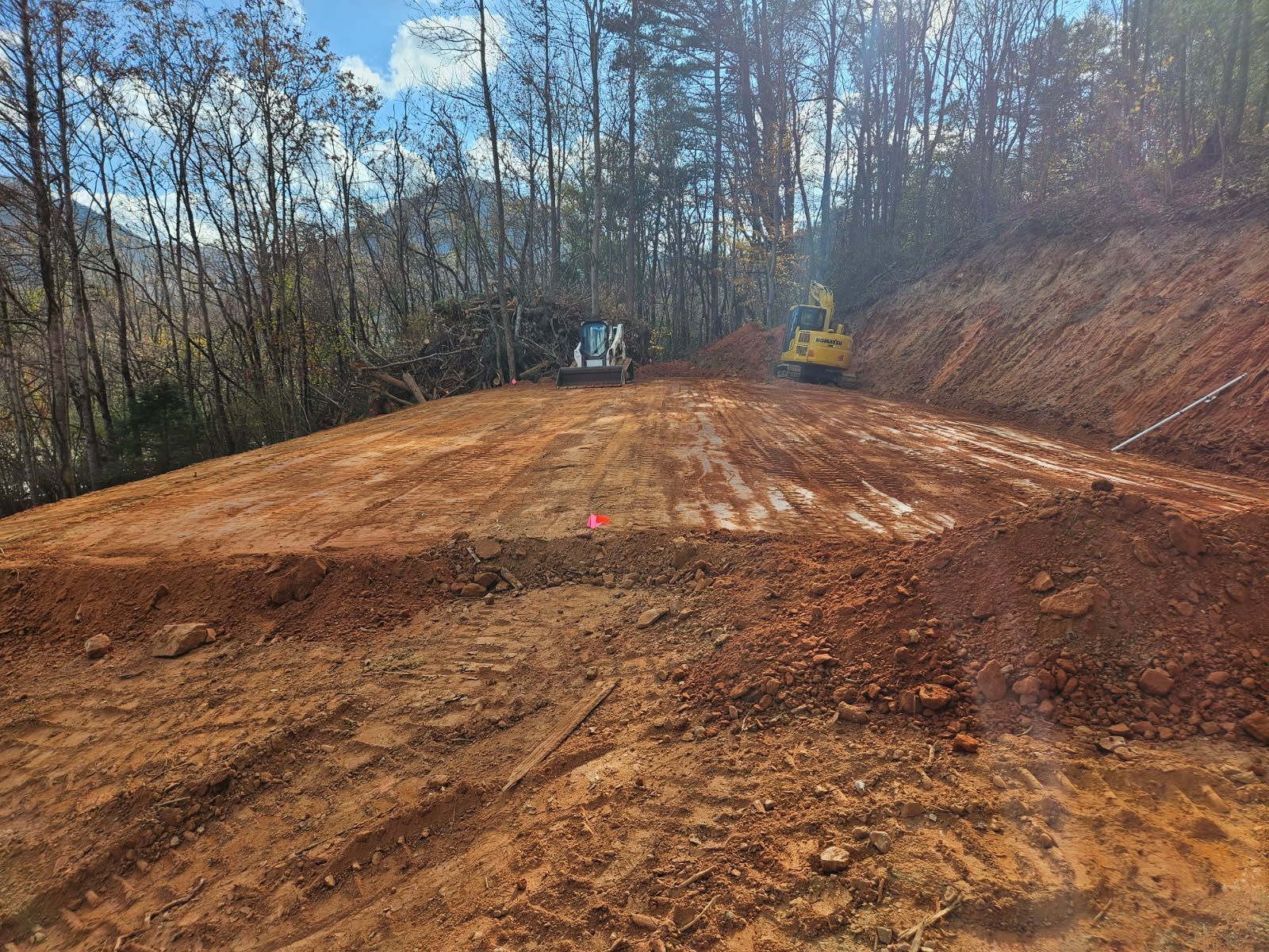 Freshly graded dirt road at a wooded construction site under a clear blue sky
