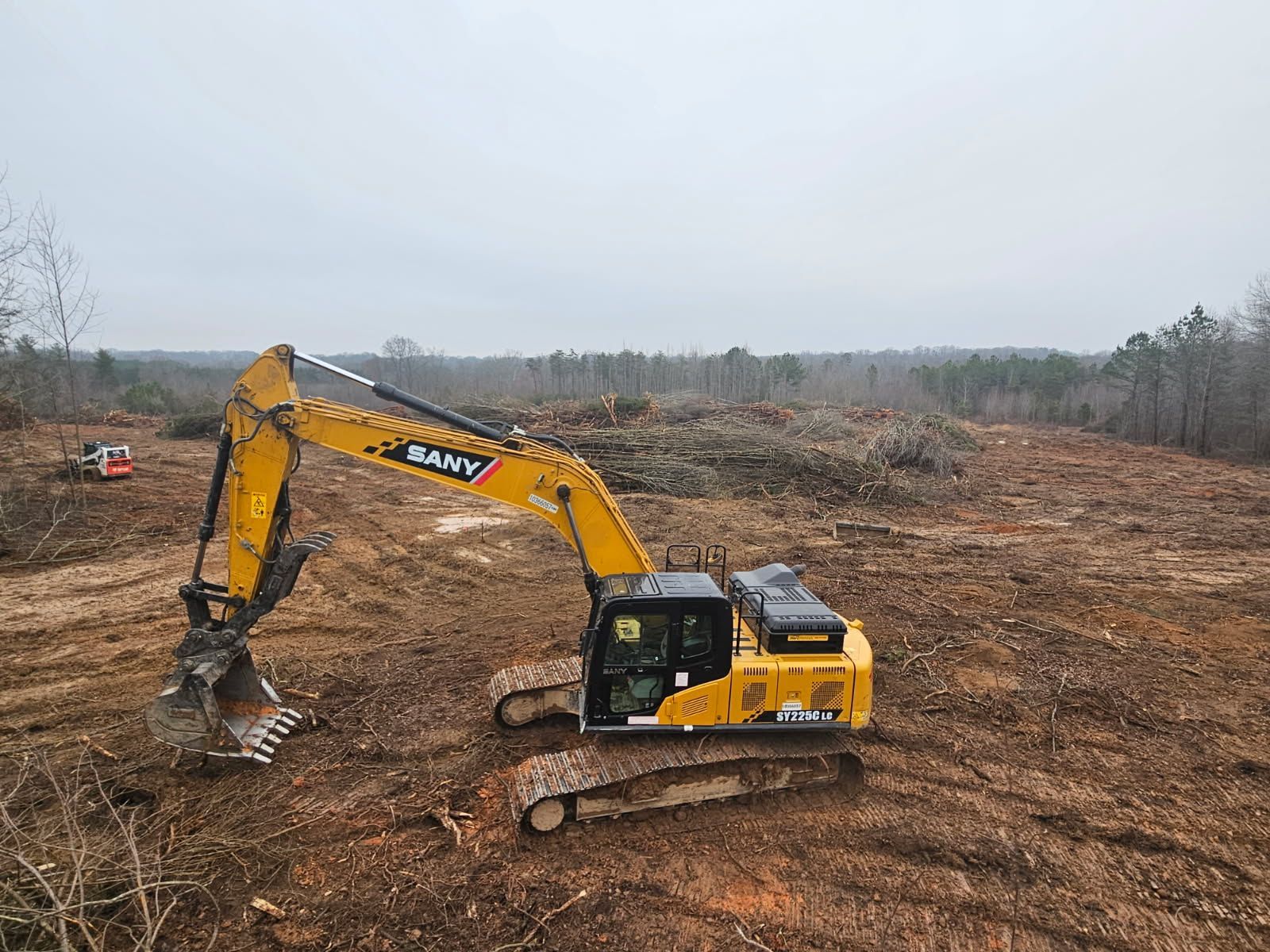 Yellow excavator working on a cleared dirt site under an overcast sky