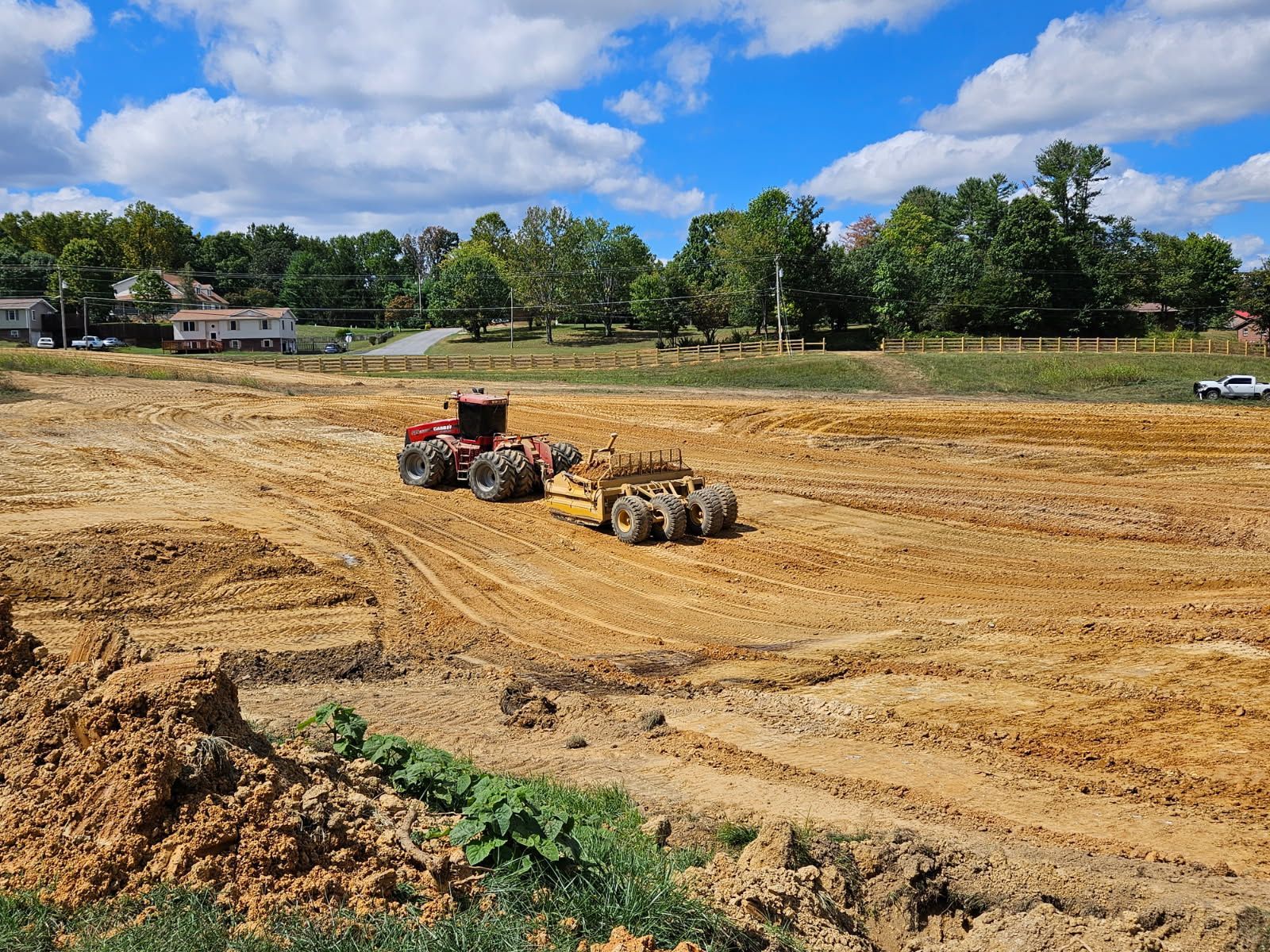 Construction site with red tractor moving dirt across a cleared field under a blue sky