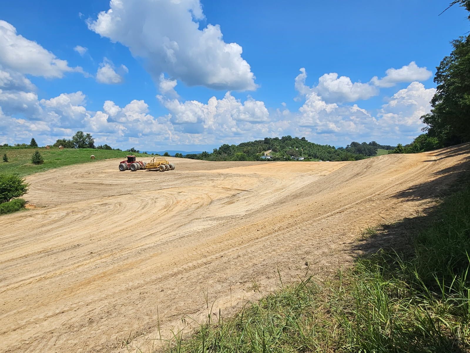 Bulldozer grading a sandy field under a blue sky with clouds