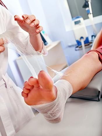 Doctor wrapping bandage around a patient's foot in a medical office.
