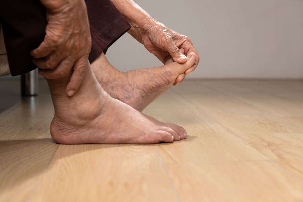 Older person holding and examining their feet, likely due to pain or discomfort.