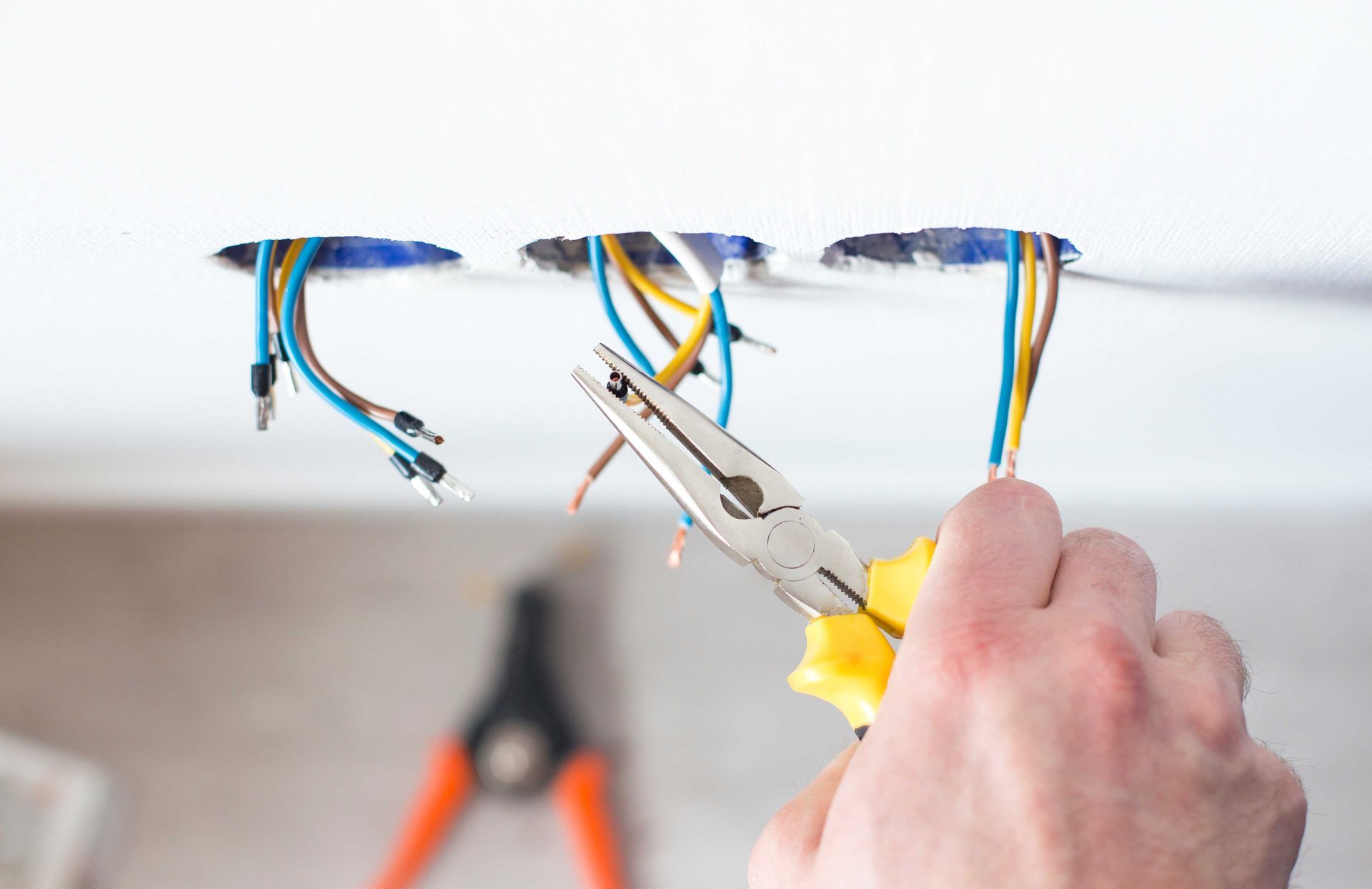 Hand using pliers to pull wires from a ceiling opening during electrical repair