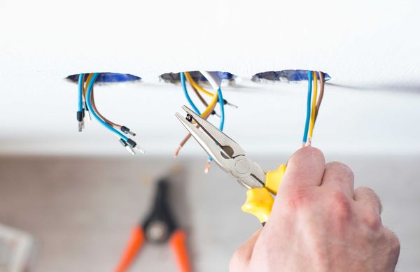 Un électricien coupe des fils électriques à l'aide d'une pince depuis une ouverture au plafond.