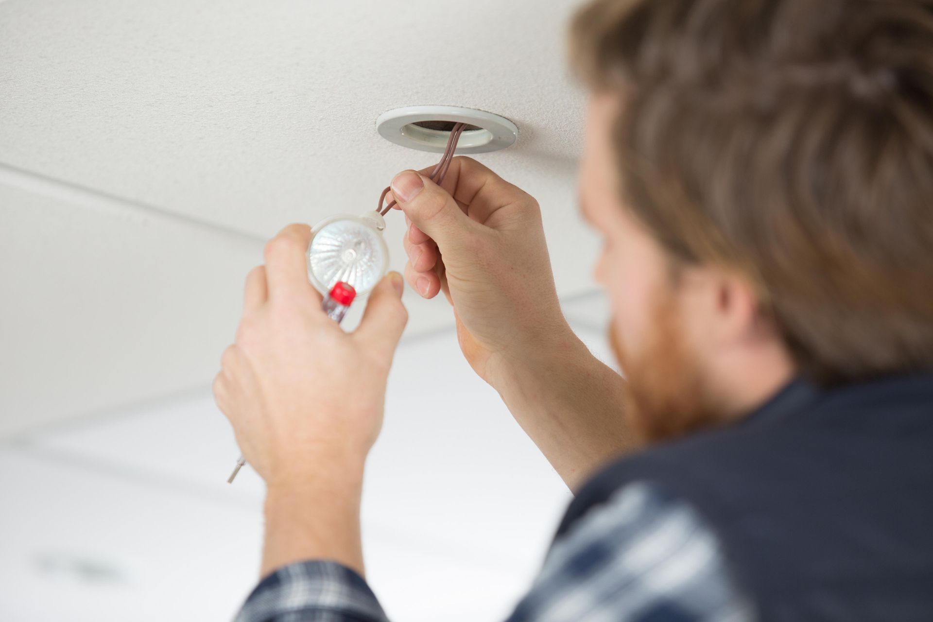 Mains installant un détecteur de fumée blanc au plafond avec un tournevis