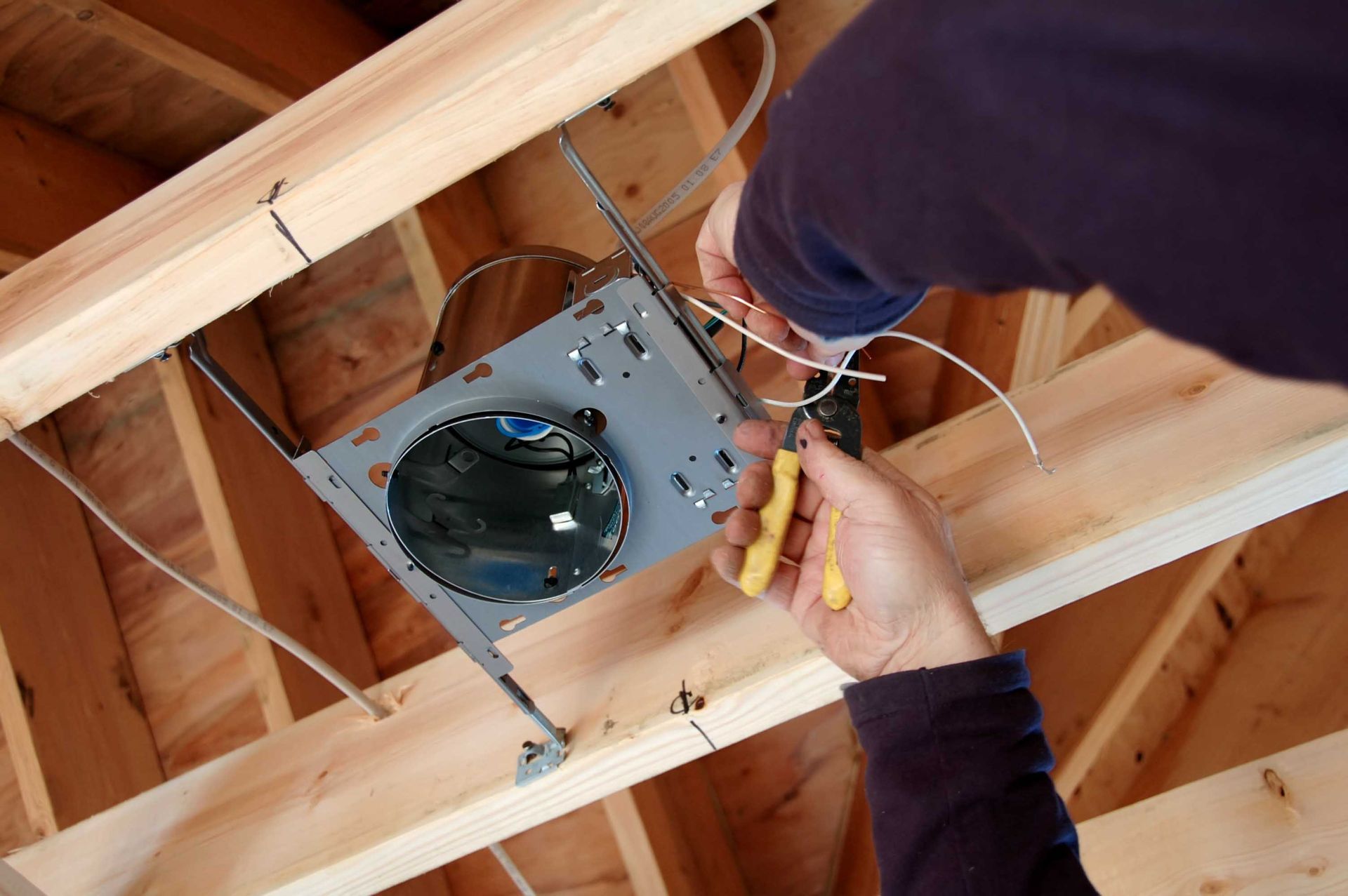 Technician wiring a ceiling fan in an unfinished attic with exposed wooden rafters