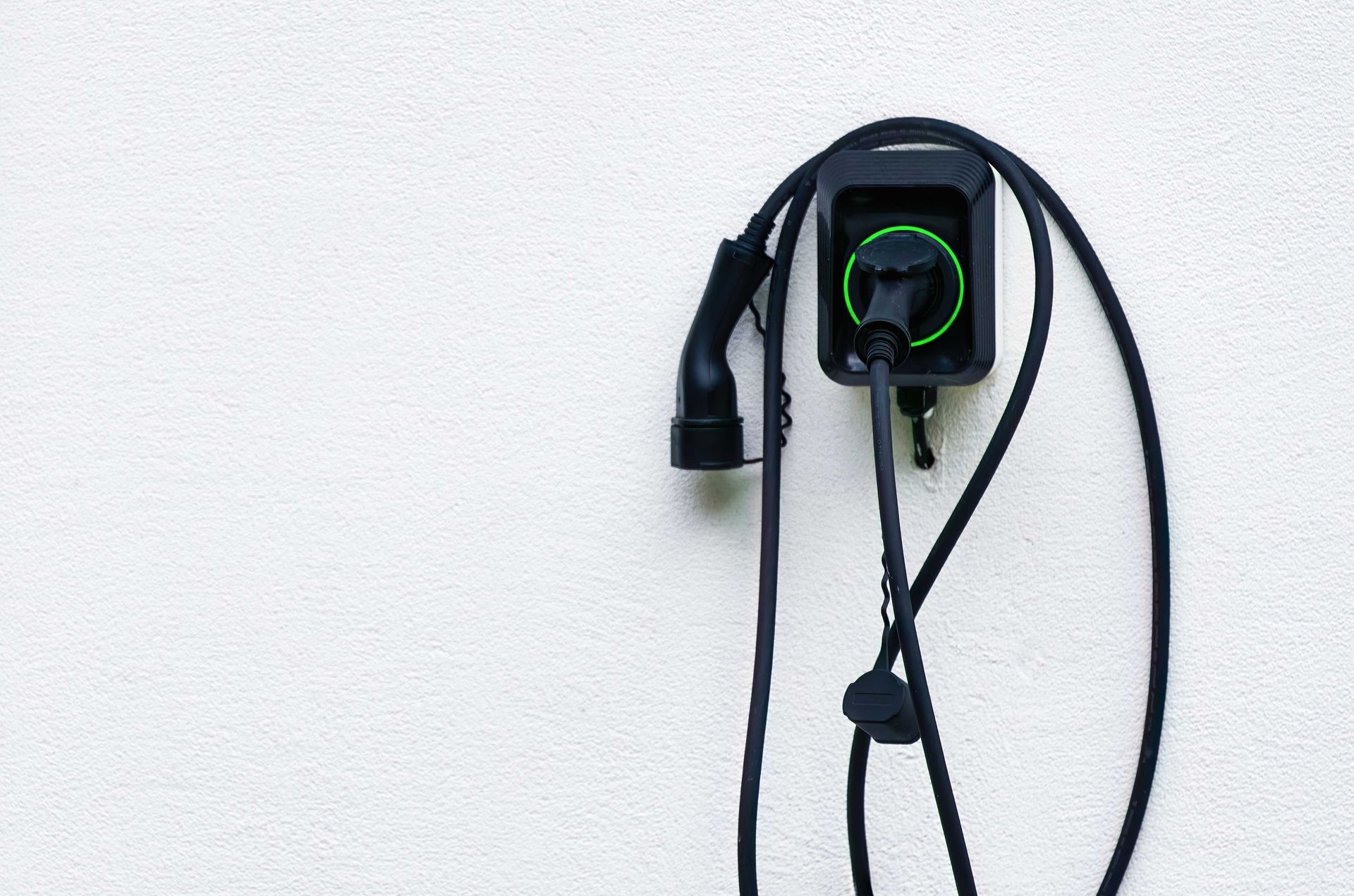 Chargeur mural noir avec un voyant vert et des câbles pendants sur un mur blanc