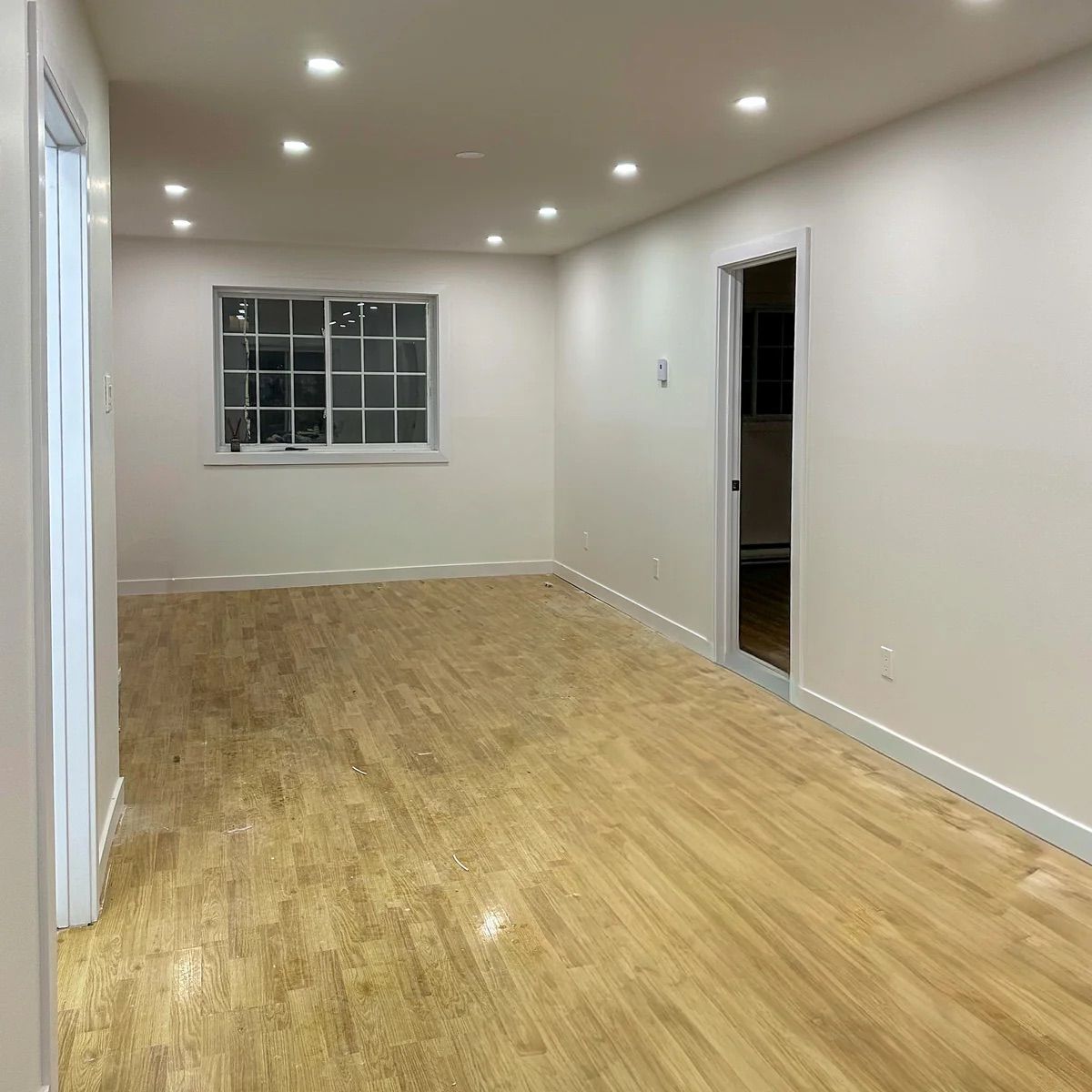 Pièce vide avec parquet clair, spots encastrés au plafond et une fenêtre sur le mur du fond.