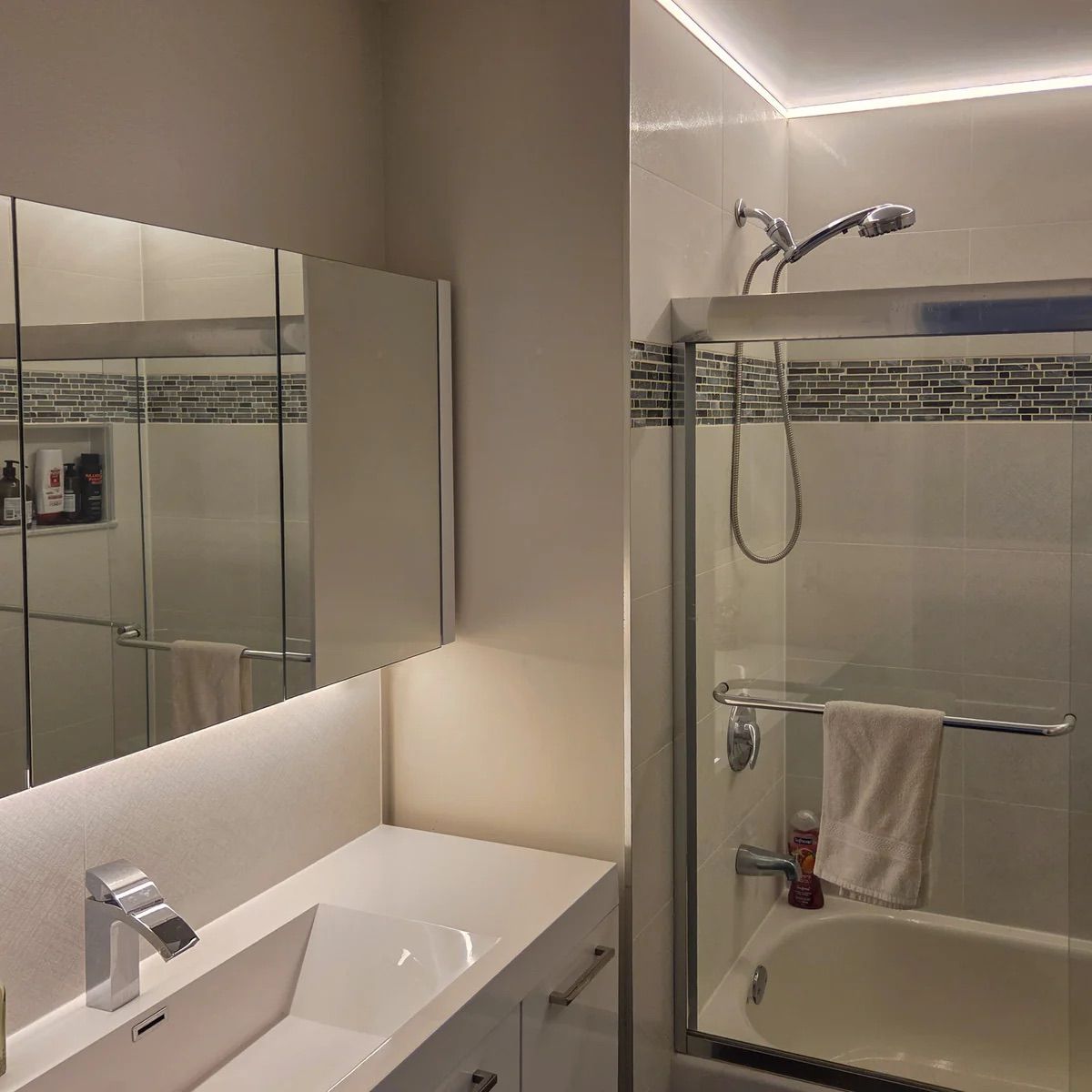 Salle de bains moderne avec miroir de courtoisie éclairé, lavabo blanc, douche en verre et porte-serviettes