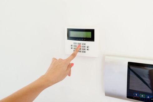 Mano che preme un termostato a parete accanto a un computer portatile su una scrivania