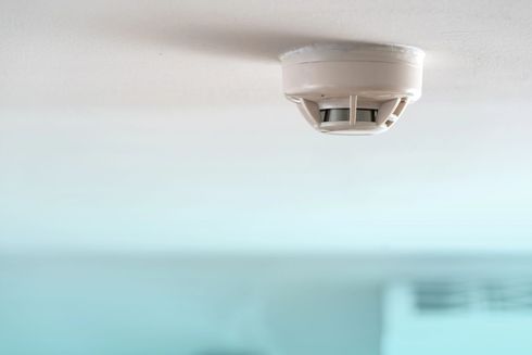 Rivelatore di fumo bianco montato a soffitto su uno sfondo chiaro e sfocato.