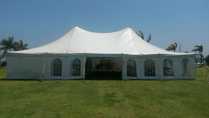 A large white marquee tent with arched windows standing on a grassy field under a clear blue sky.