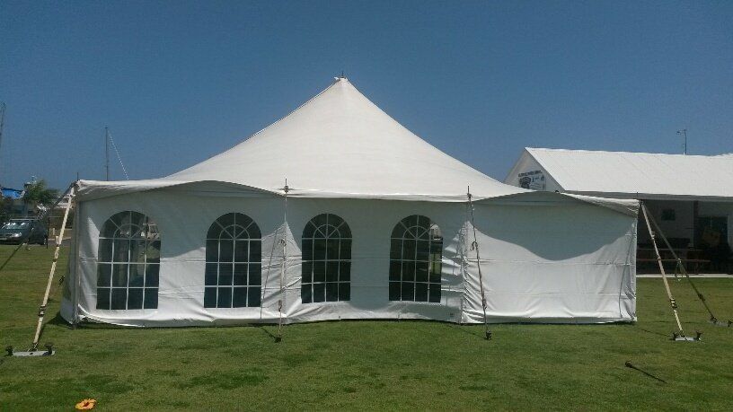 A large white pole tent with arched windows standing on a grassy field under a clear blue sky.