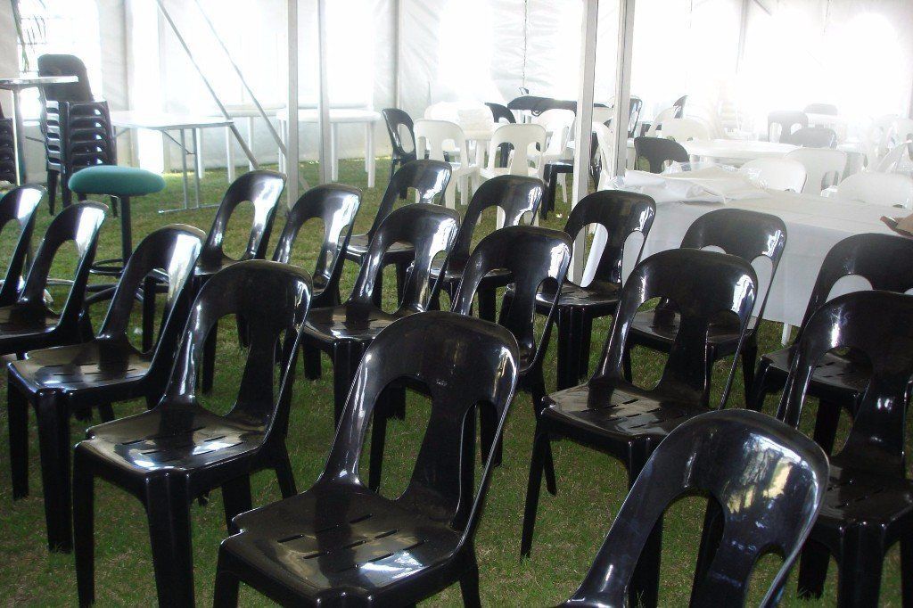 Rows of black plastic chairs arranged on grass under a large white tent.