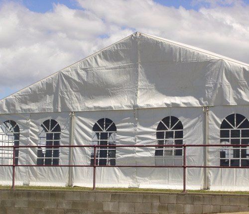 A large, white temporary event tent with arched windows, set against a blue sky with clouds.