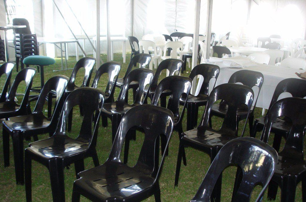 Rows of black plastic chairs arranged for an event under a white tent on a grassy surface.