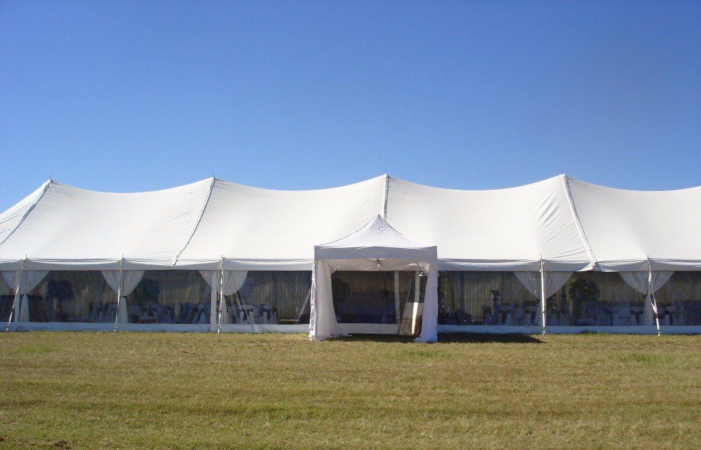 A large white event tent with clear sidewalls sits on a grassy field under a clear blue sky.