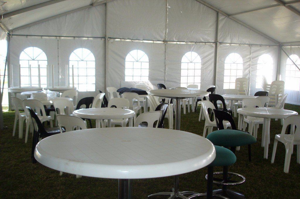 White plastic tables and chairs arranged inside a large event tent with arched windows.