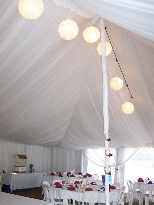 A white marquee tent interior decorated with hanging paper lanterns and set tables for a reception.