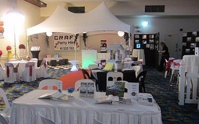 Event space featuring a central white canopy tent, round and rectangular tables with white cloths, and party displays.