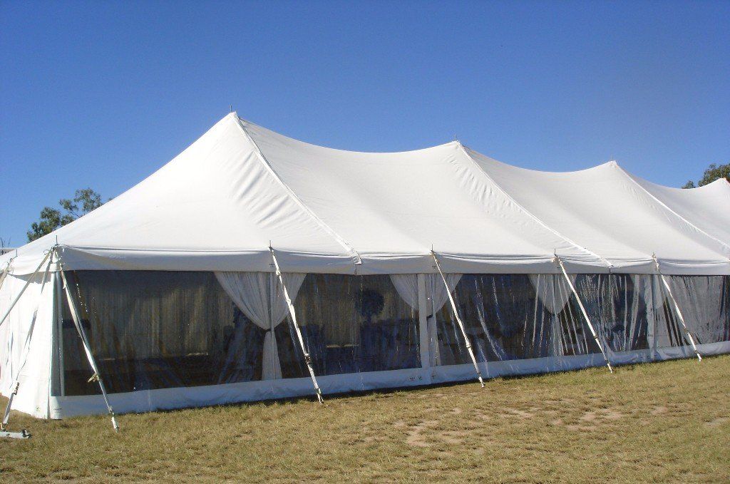A large white event tent with clear sidewalls set up on a grassy field under a clear blue sky.