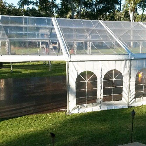 A large, white wedding-style tent with clear plastic roof panels and arched windows sits on a green lawn.