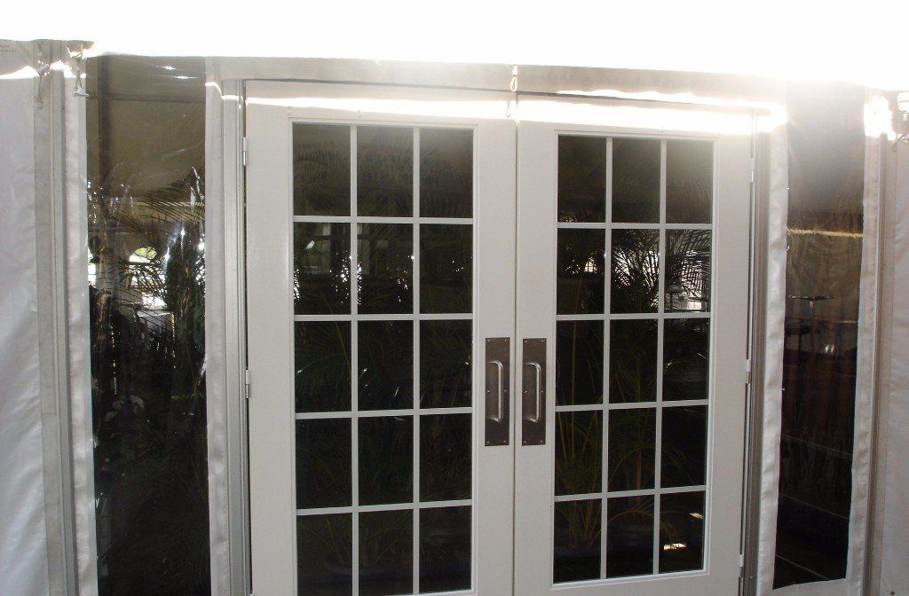A pair of white, grid-paned French doors set within a tent wall, featuring silver vertical pull handles.