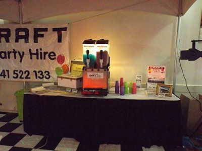 A party rental booth featuring a slushy machine with two flavors, cups, and a banner reading 