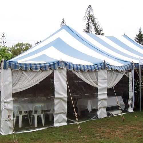A large blue and white striped party tent with transparent sidewalls, draped white curtains, and tables with chairs.