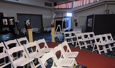 Rows of empty white folding chairs set up in a room for an event, facing a display area with a chalkboard and curtains.