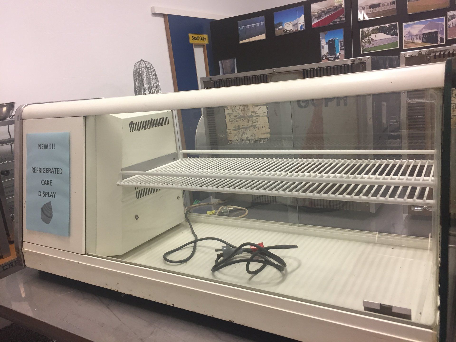 A white, countertop-style display case with a glass front, one internal metal shelf, and a power cord on the floor.