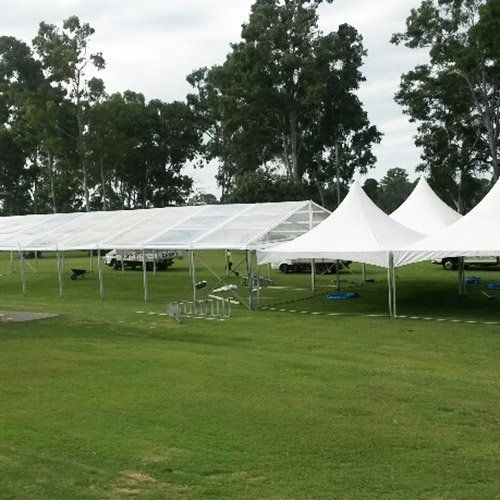 Large white event tents set up on a grassy field in front of a tree line.
