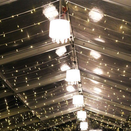 A row of white drum pendant lights hangs from the interior of a dark, tented ceiling illuminated by strings of fairy lights.