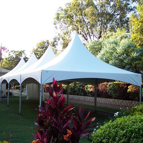 Four connected, pointed white peaked tents set up in a garden with green lawns and trees.