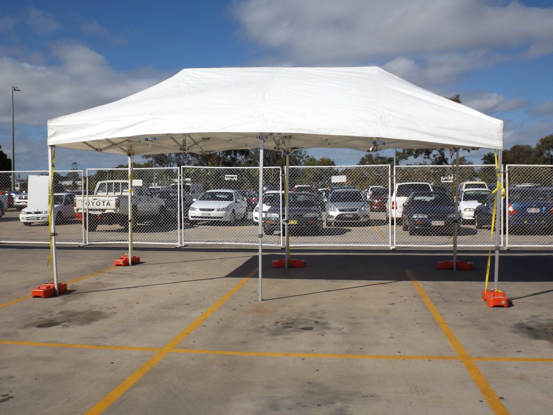 A large, white pop-up canopy tent set up on an asphalt parking lot with parked cars in the background.