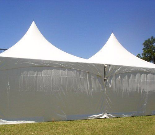 Two large white peak-style event tents connected side-by-side on a grassy lawn under a clear blue sky.