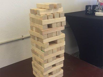 A Jenga tower made of rectangular wooden blocks stacked on a table in an indoor setting.