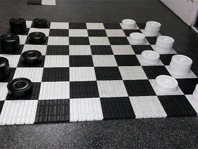 A giant floor-based checkers game set with black and white pieces on a checkered board.