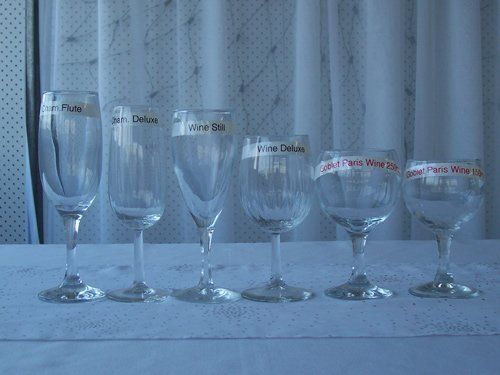 Six different-sized wine glasses lined up on a white tablecloth in front of a white curtain.