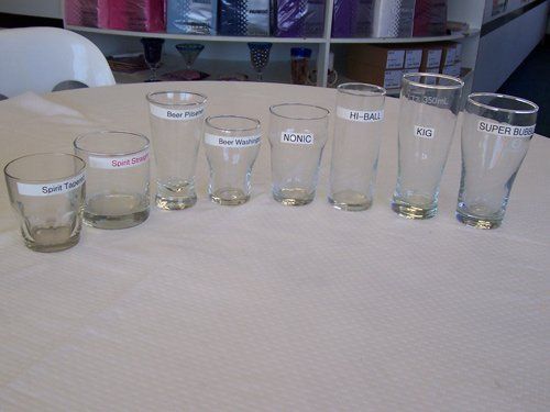 Eight labeled drinking glasses of various sizes and shapes are arranged in a row on a white tablecloth.