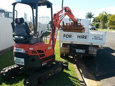 An orange Kubota excavator sits on grass next to a white truck with
